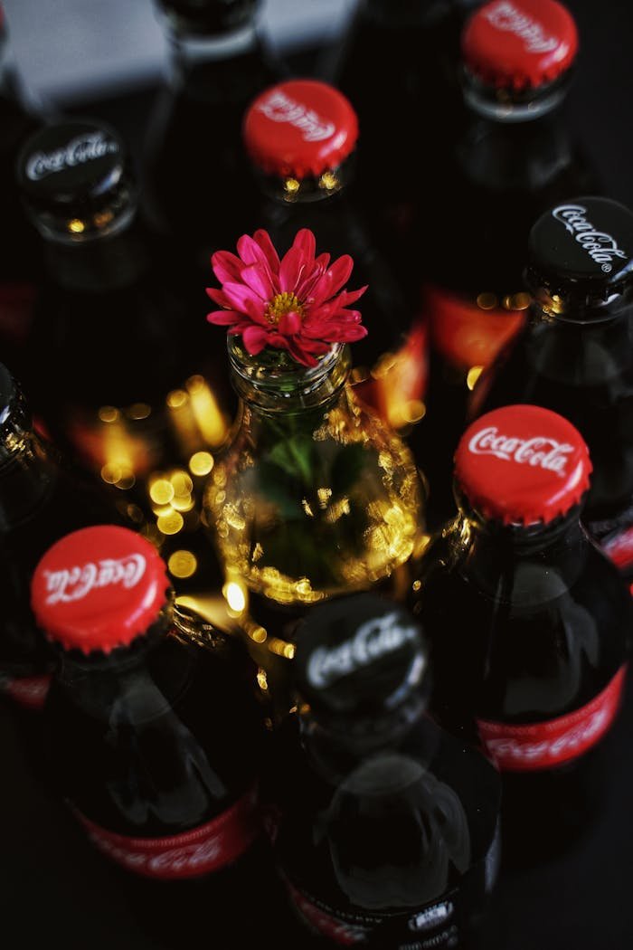 Creative arrangement of Coca-Cola bottles with a pink flower centerpiece and bokeh lighting.